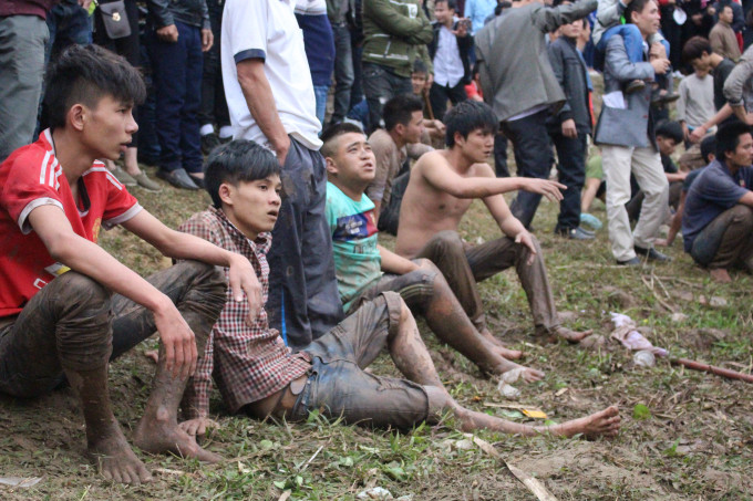Một nhóm thanh niên bỏ cuộc ngồi bệt trên bờ ruộng nhìn đám đông tranh giành phết